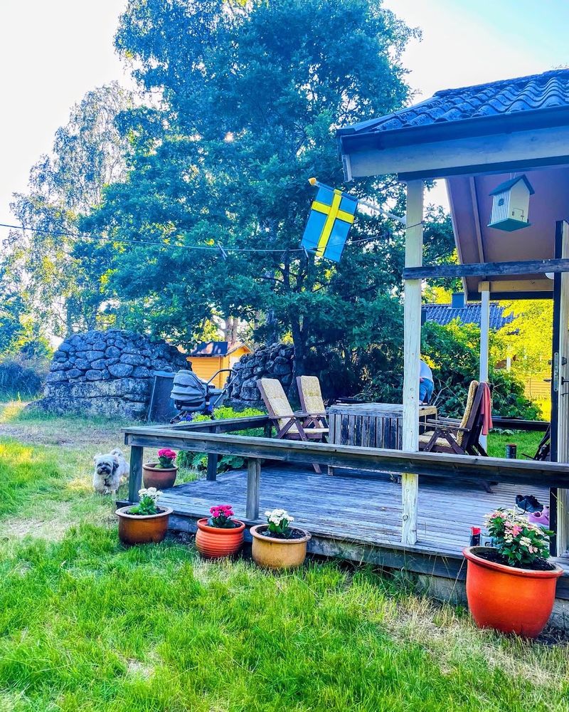 Terrasse mit Gartenstühlen und Blumentöpfen auf dem Rasen vor der Stuga Eos im Sommer